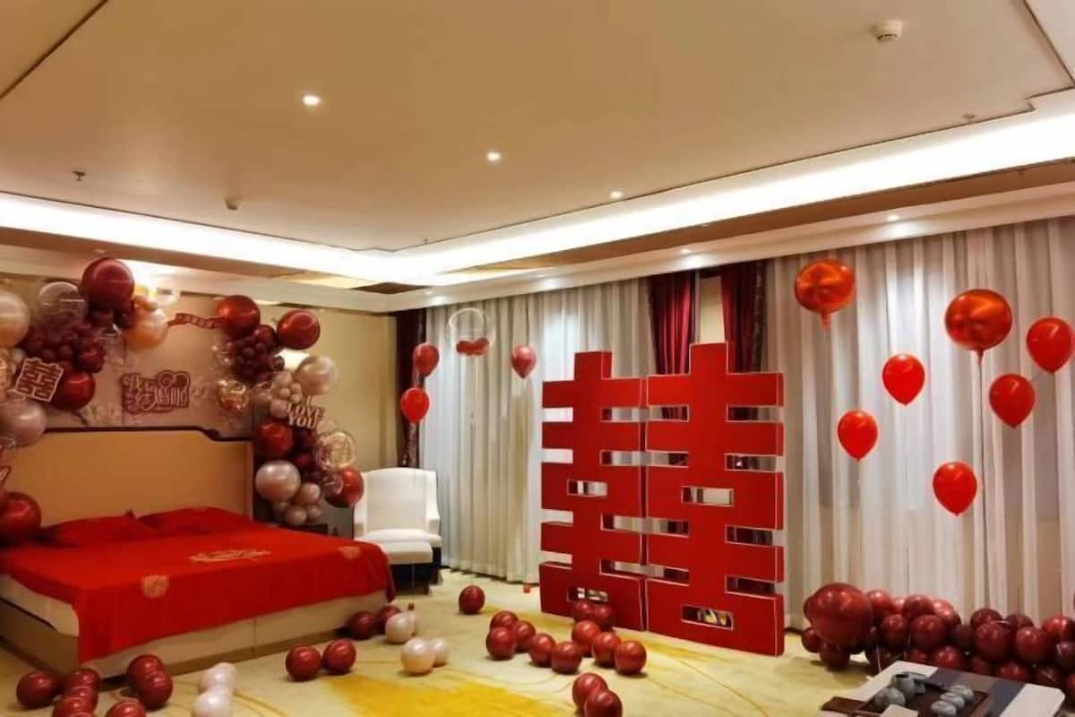 A hotel room with a bed, a white chair, a red partition, and balloons.