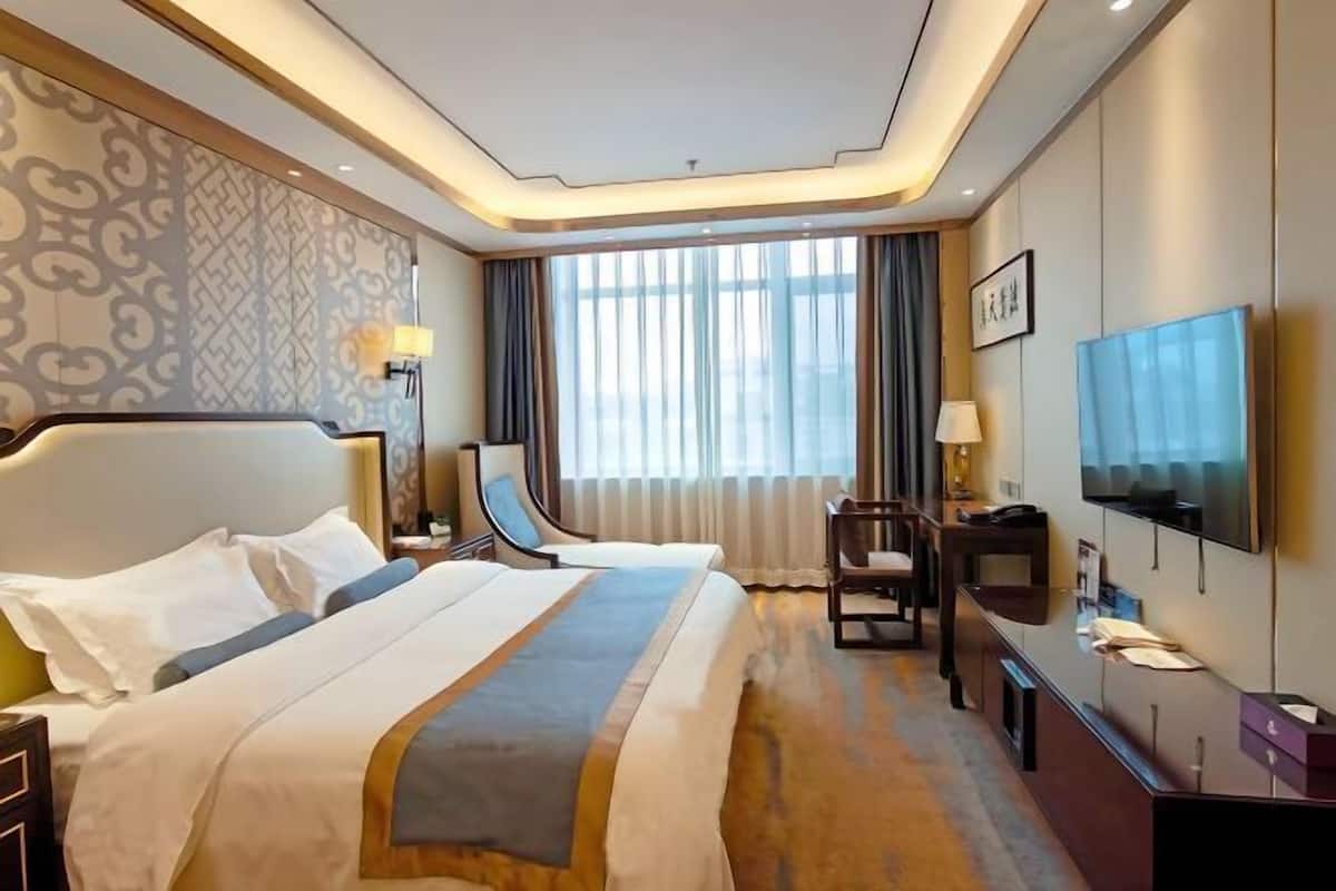A hotel room with a large bed, a desk, a chair, a TV, and a window with curtains.