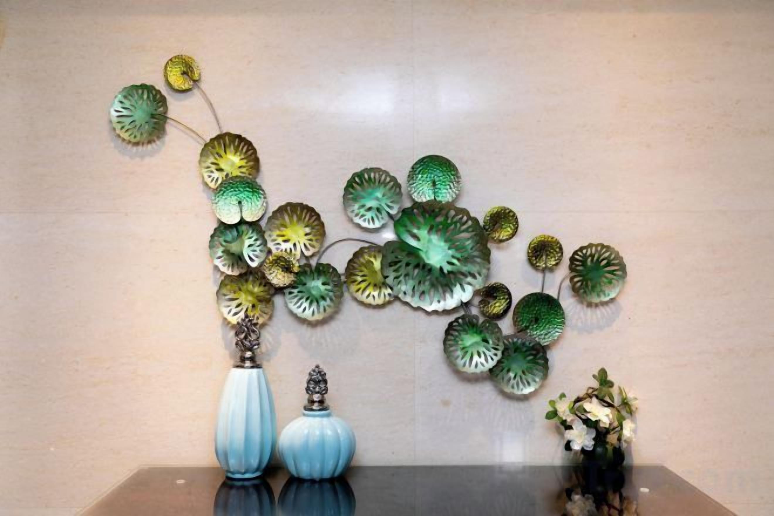 A wall with decorative glass art and two vases on a reflective surface.