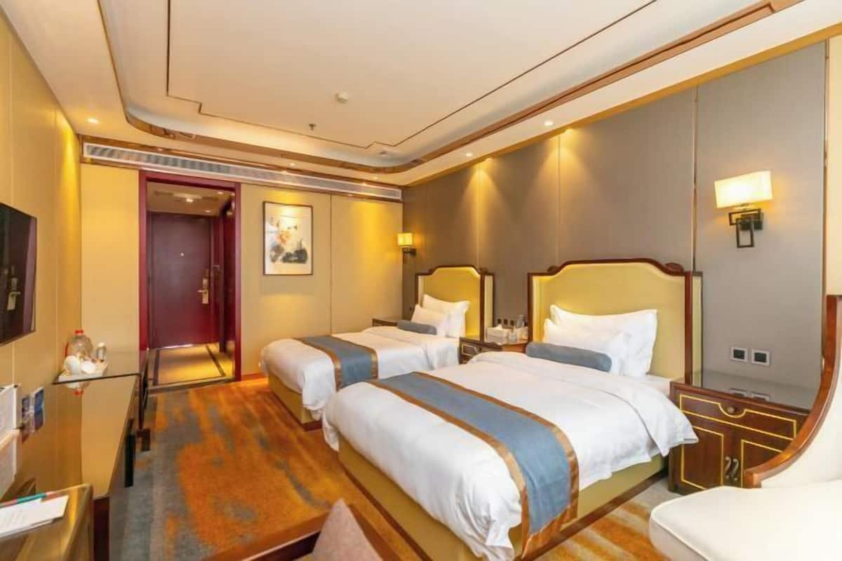 A hotel room with two beds, a desk, a chair, a TV, and a door.