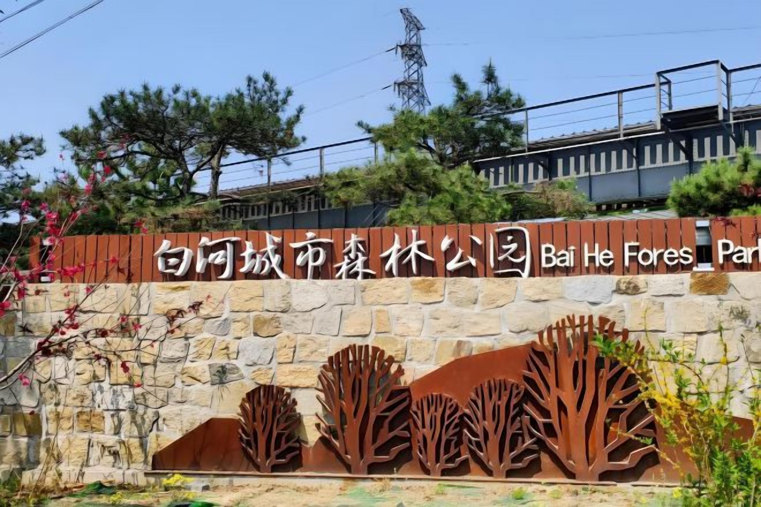 A stone wall with a metal tree sculpture and a sign in a foreign language.