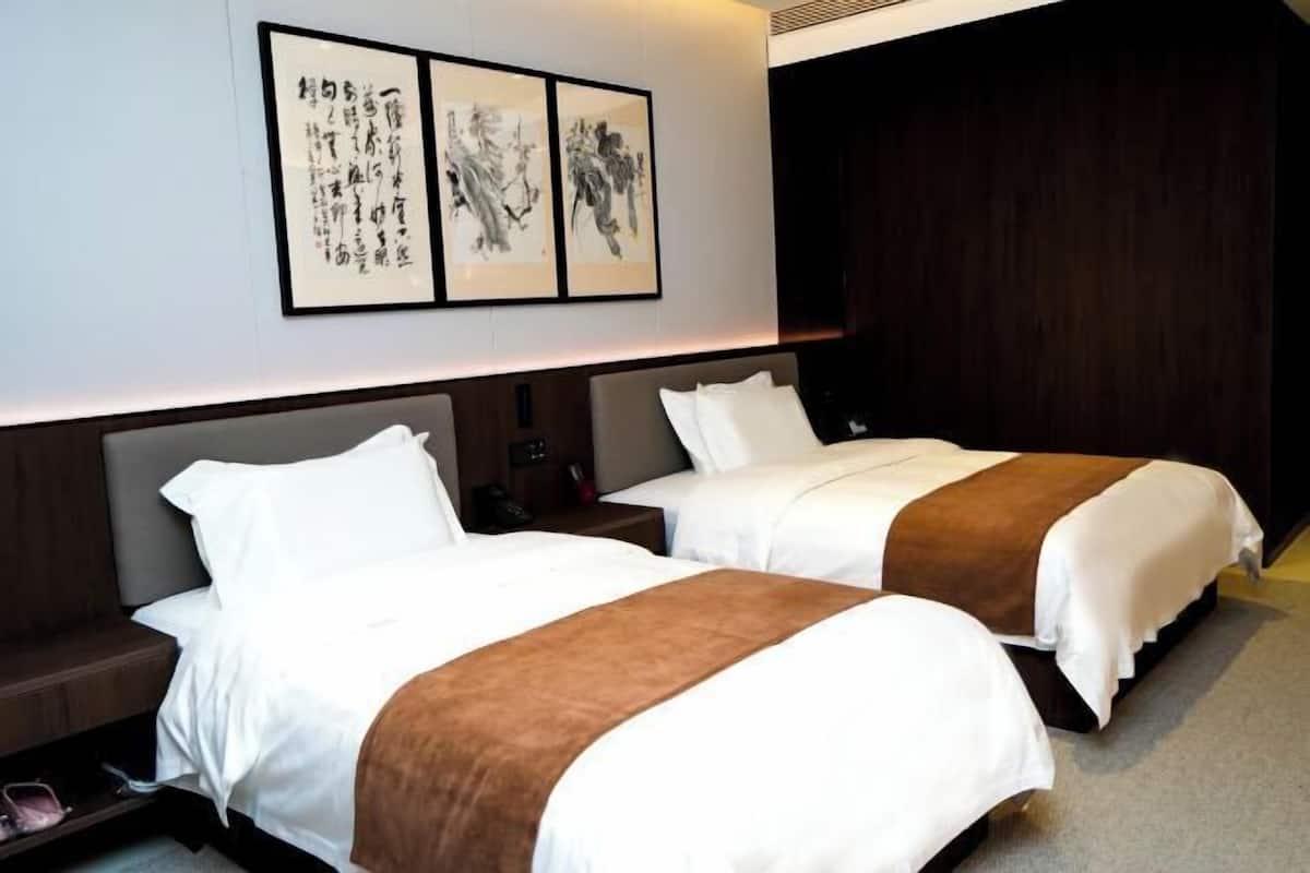 A hotel room with two beds, a dark wooden headboard, a wall-mounted artwork, and a shoe rack.