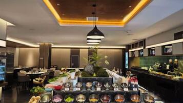 A buffet area with multiple food stations, a modern chandelier, and a seating area with tables and chairs.