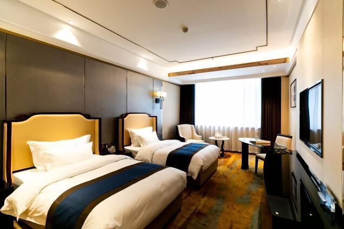A hotel room with two beds, a TV, a small table, and a window with curtains.