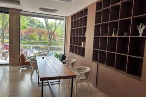 A modern interior with a long wooden table and chairs, a large window with a view of the outside, and a wall with shelves. - Qiu shan Hotel (Wenzhou)