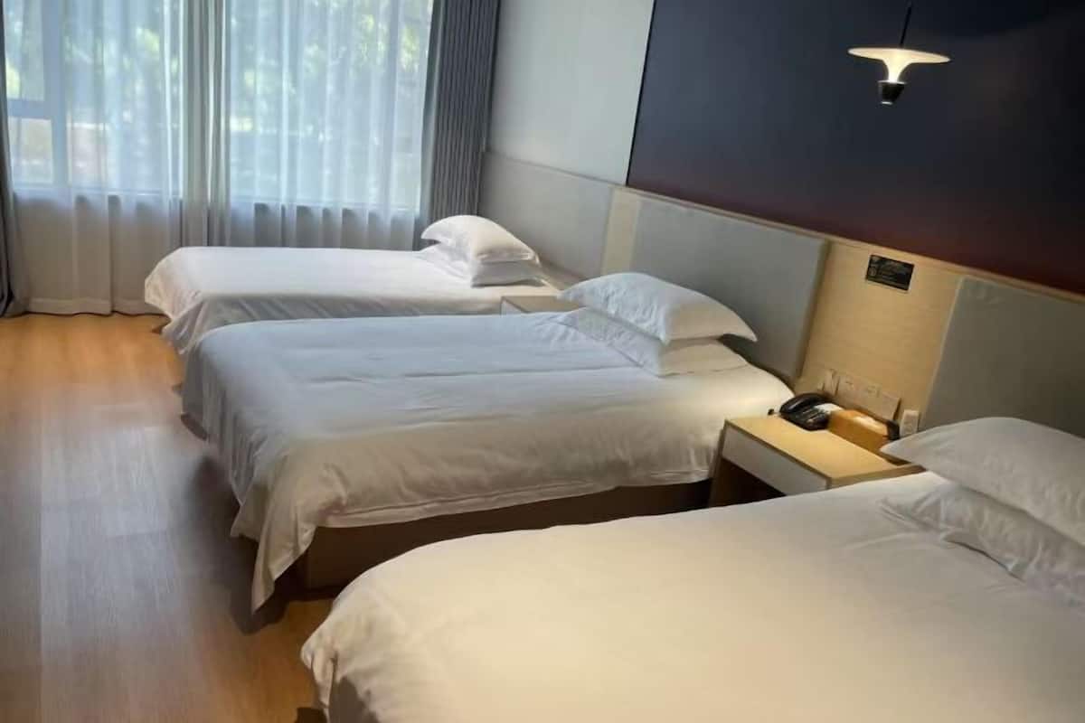 A hotel room with three beds, a bedside table with a phone, and a wall-mounted light fixture.