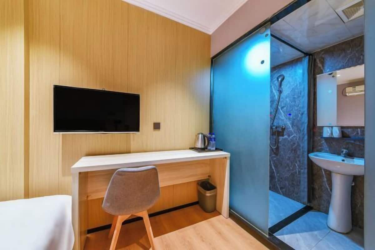 A modern bathroom with a shower, sink, and a flat-screen TV mounted on the wall.