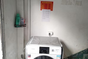 A room with a washing machine, a shelf with cleaning supplies, and a wall with a notice. - Qiu shan Hotel (Wenzhou)