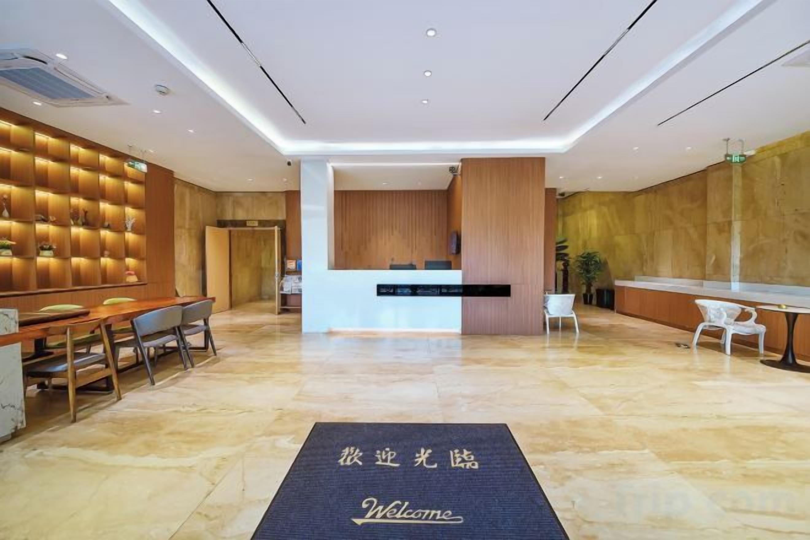 Zona de recepción de un hotel con mostrador, área de descanso y felpudo de bienvenida.
