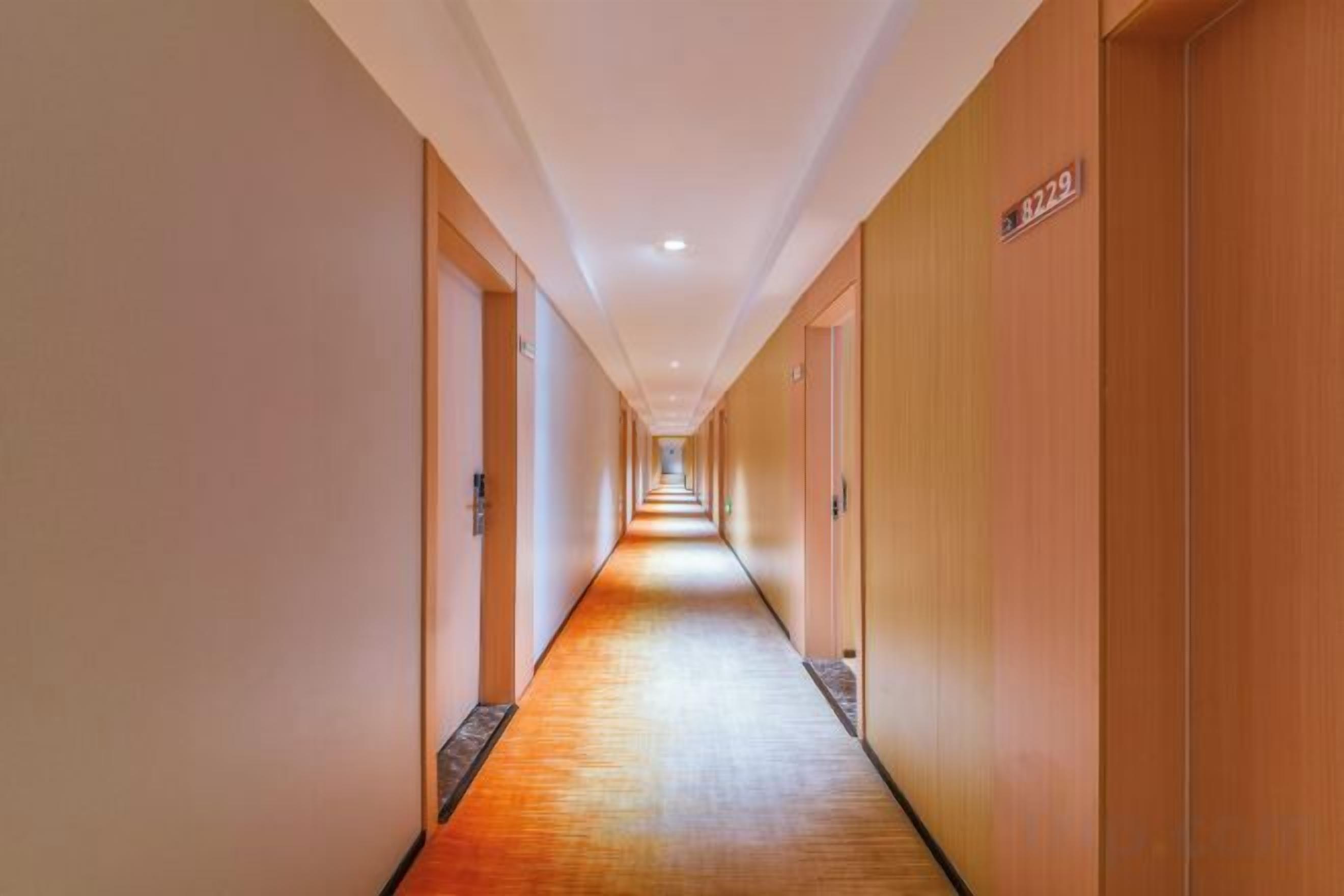 A long, narrow hotel corridor with doors on both sides, a wooden floor, and a sign indicating room number 8229.