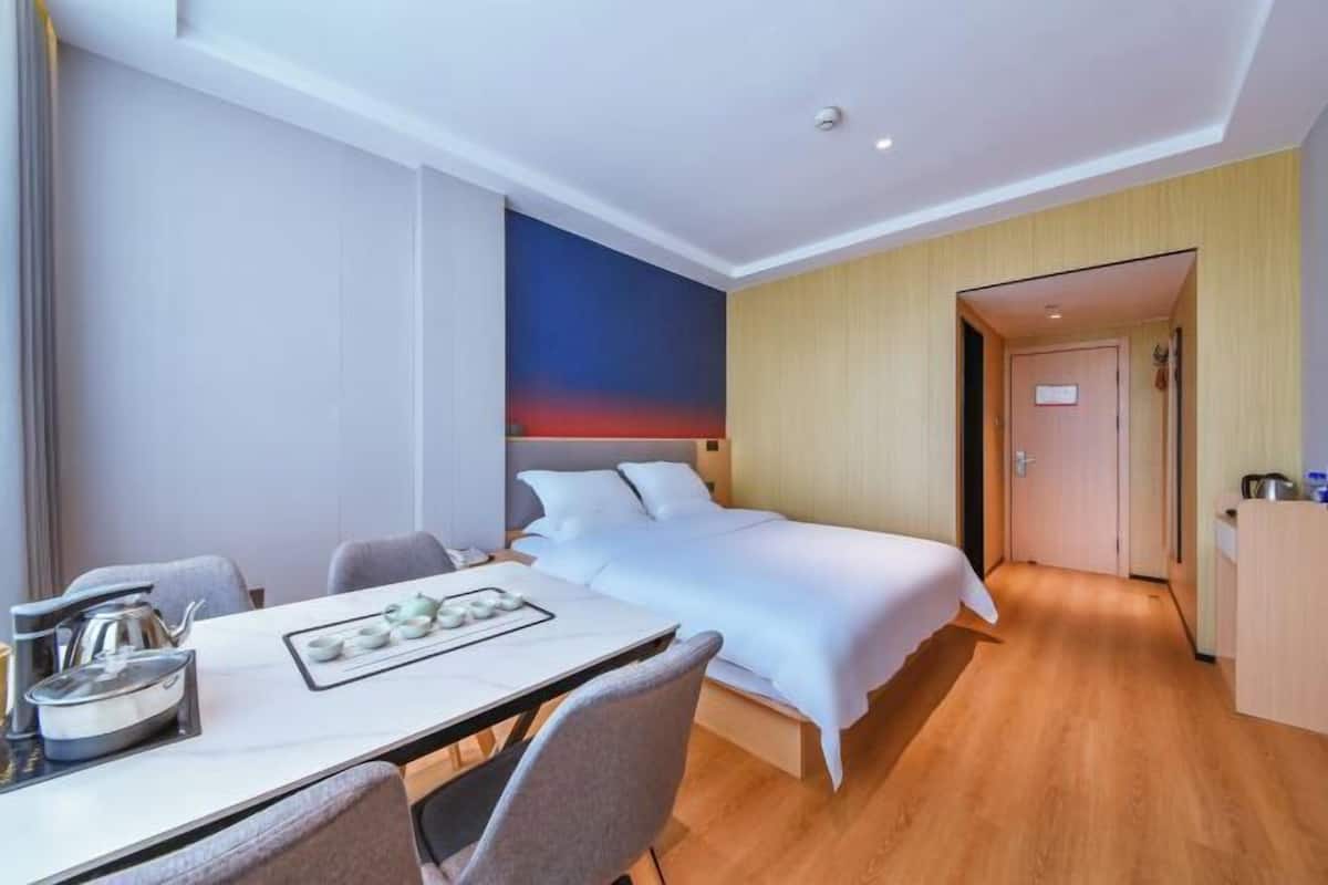 A hotel room with a bed, a dining table with chairs, a kitchen area, and a bathroom.