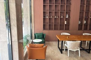A room with a wooden table, chairs, a green sofa, and a shelving unit with decorative items.