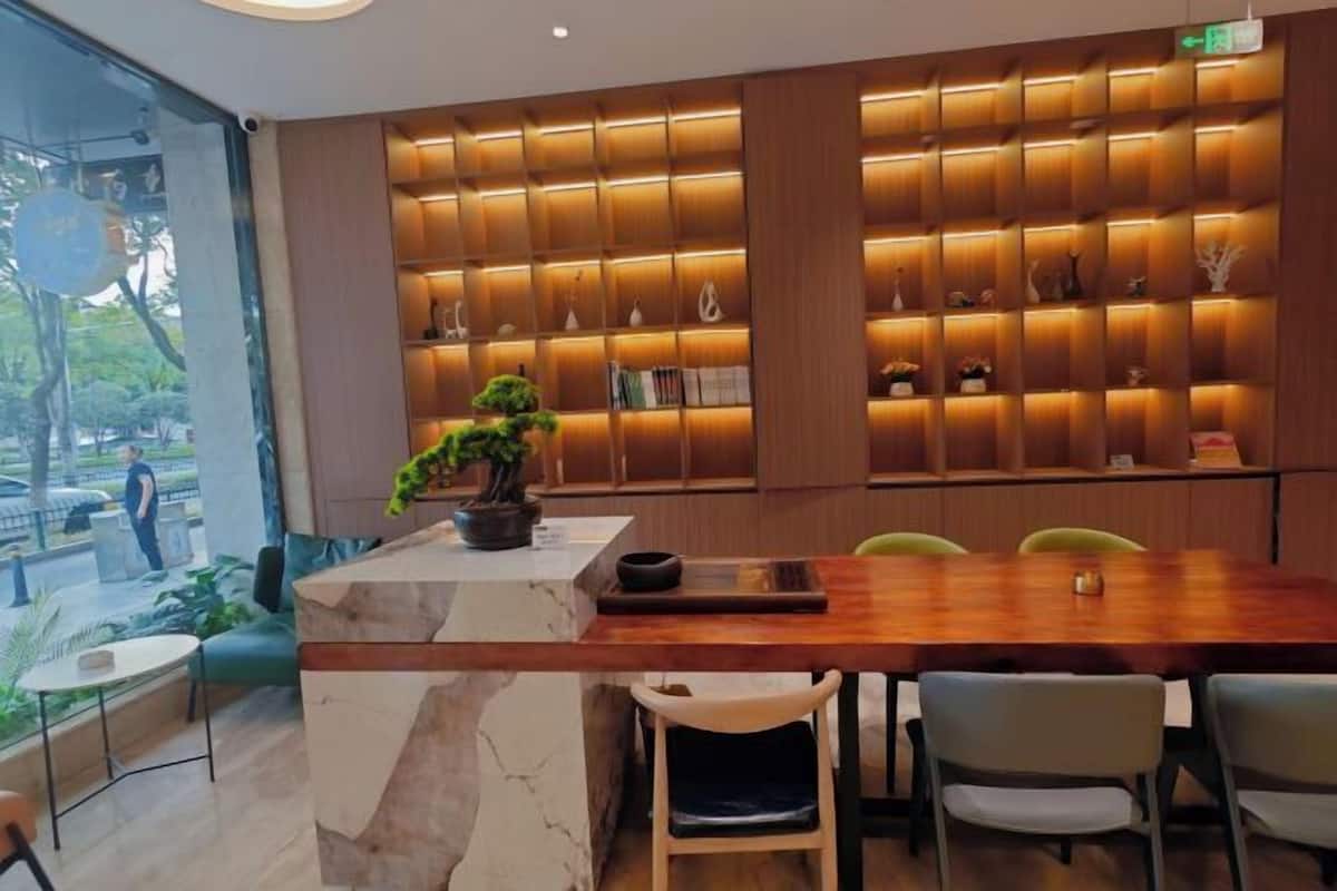 A modern interior with a marble reception desk, a wooden dining table, and a wall of illuminated shelves.