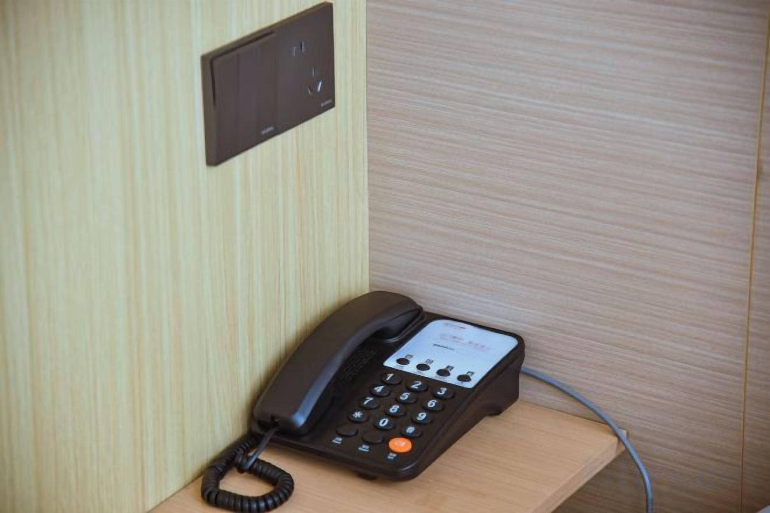 A black telephone on a wooden desk with a cord plugged in.