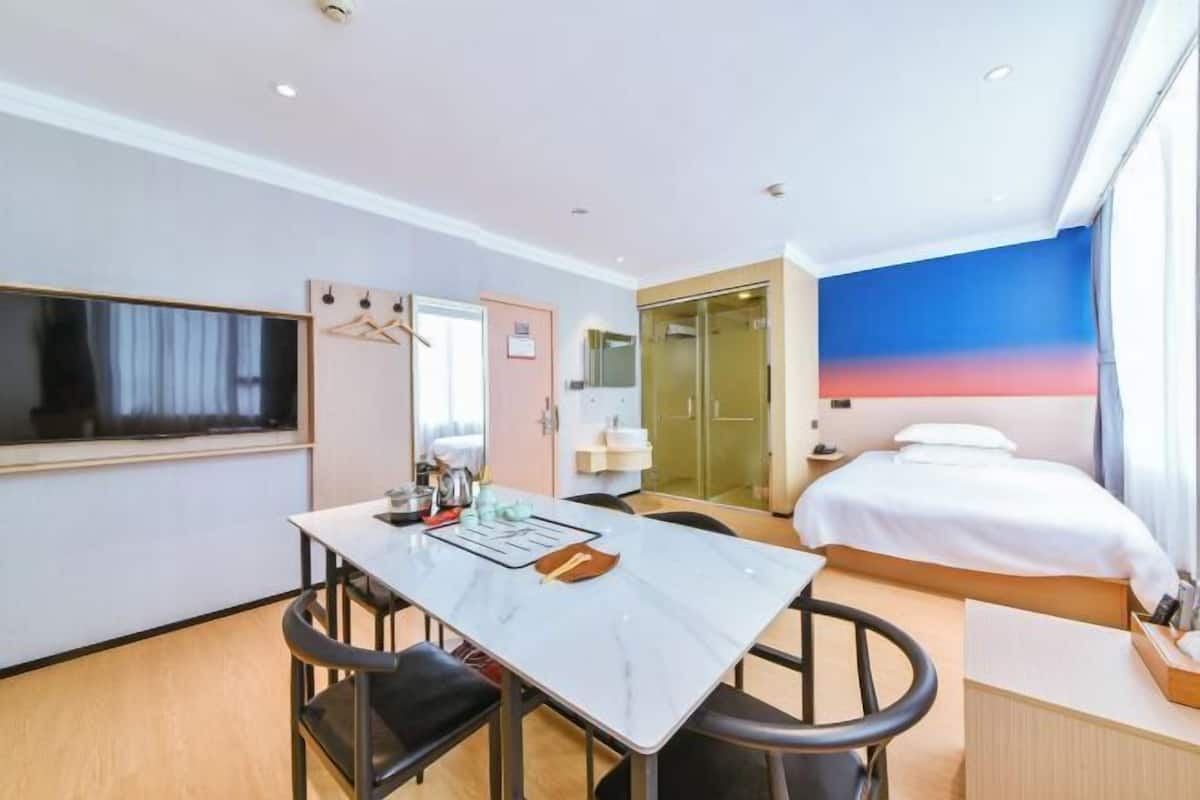A hotel room with a bed, a desk with chairs, a television, and a large window with a view.