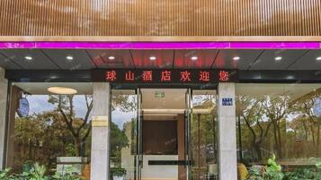 A hotel entrance with a sign in Chinese characters, glass doors, and a reflection of trees and sky.