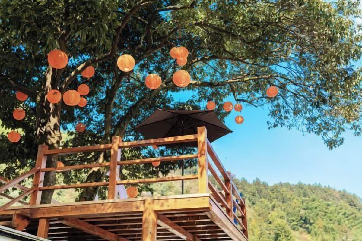 A wooden deck with a railing, an umbrella, and hanging lanterns.