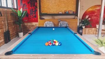A pool table with balls, two chairs, a red wall with Chinese characters, and a wooden wall with shelves.