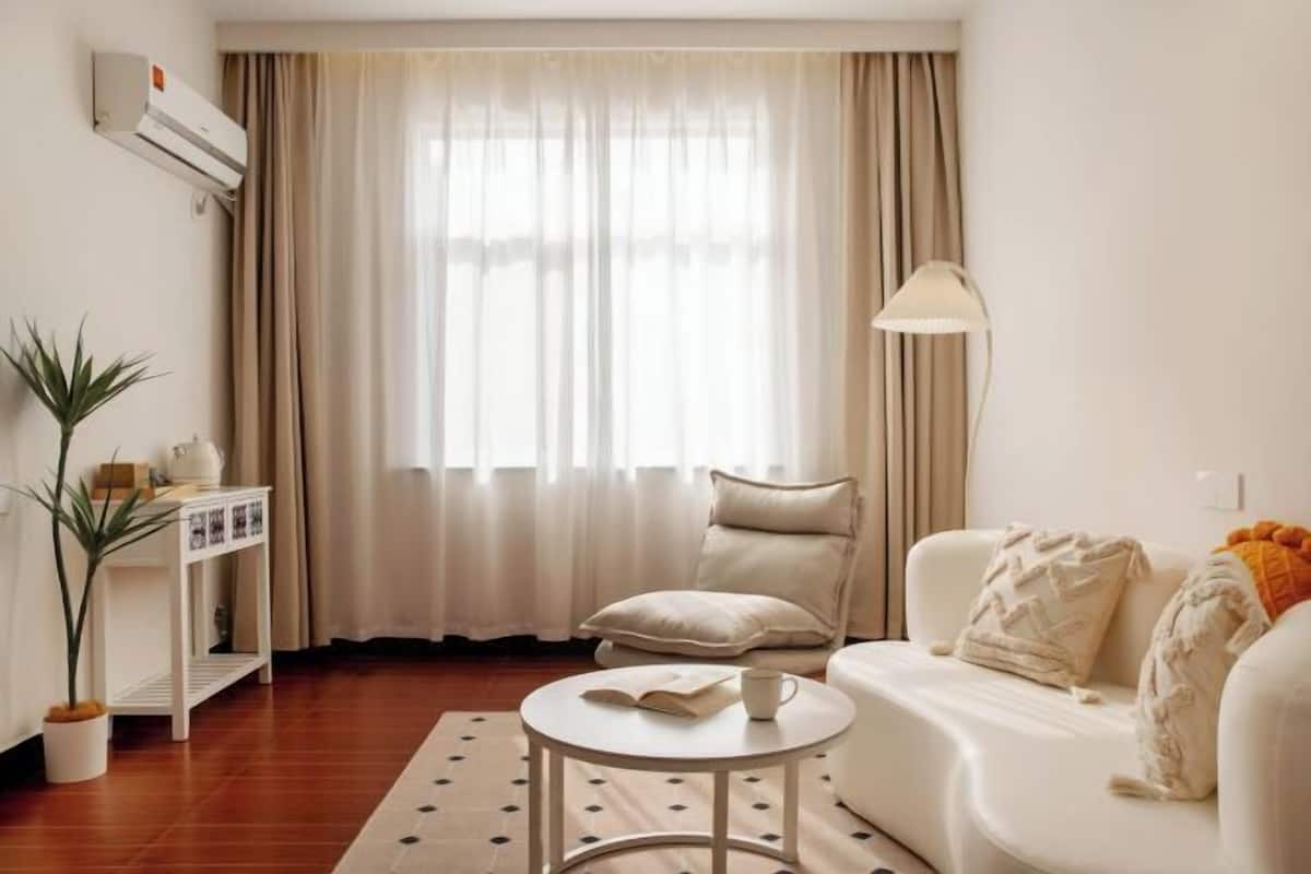 A living room with a white sofa, a round coffee table, a beige armchair, a potted plant, and a lamp.