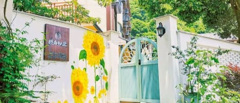 A building entrance with a sunflower mural, a blue gate, and a stone pathway.