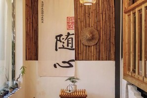 Un interior tradicional con una gran obra de caligrafía, un panel de pared de bambú y una pequeña mesa de madera con una planta.