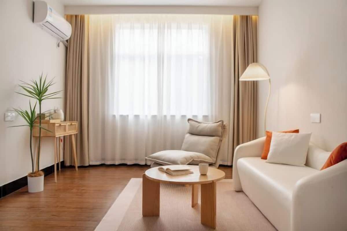 A modern living room with a sofa, a coffee table, a chair, a lamp, and a window with curtains.
