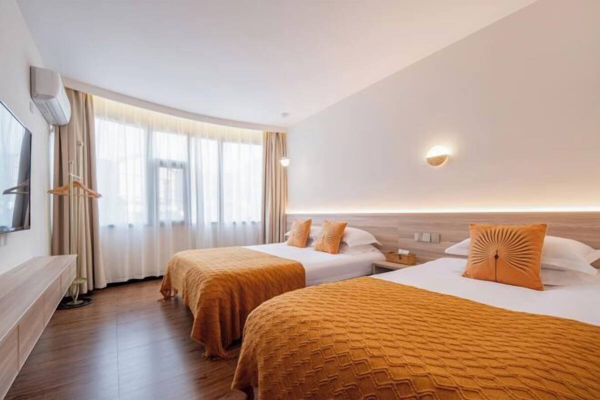 A hotel room with two beds, a TV, a desk, and a window with curtains.
