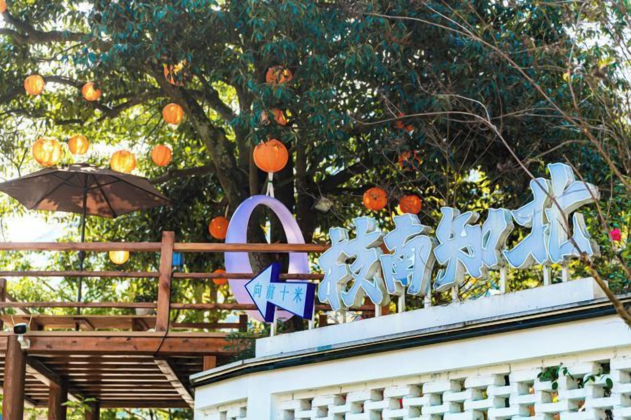 Une enseigne avec des caractères chinois, une structure en bois et un arbre décoré de lanternes suspendues.