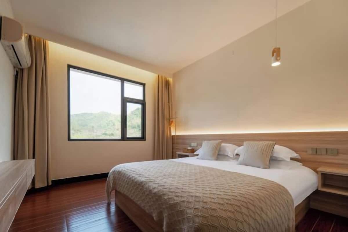 A hotel room with a large bed, a window with curtains, a bedside table, and a wall-mounted light fixture.