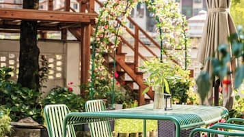 Un área de estar al aire libre con una mesa y sillas, rodeada de plantas y una estructura de madera.