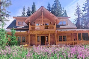 Une cabane en rondins dotée d’un balcon, de grandes fenêtres et d’une véranda.