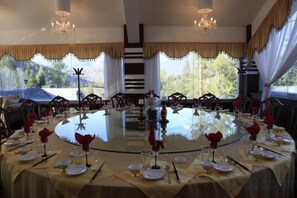 A round dining table set for a meal with chairs around it, large windows with curtains, and a chandelier. - The Four Seasons Amusement Hotel Kanas (Burqin)