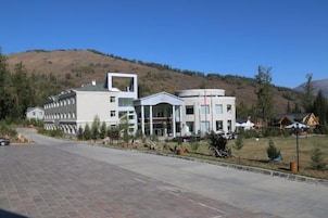 Un edificio moderno con un atrio central, rodeado de una zona pavimentada y un paisaje montañoso.