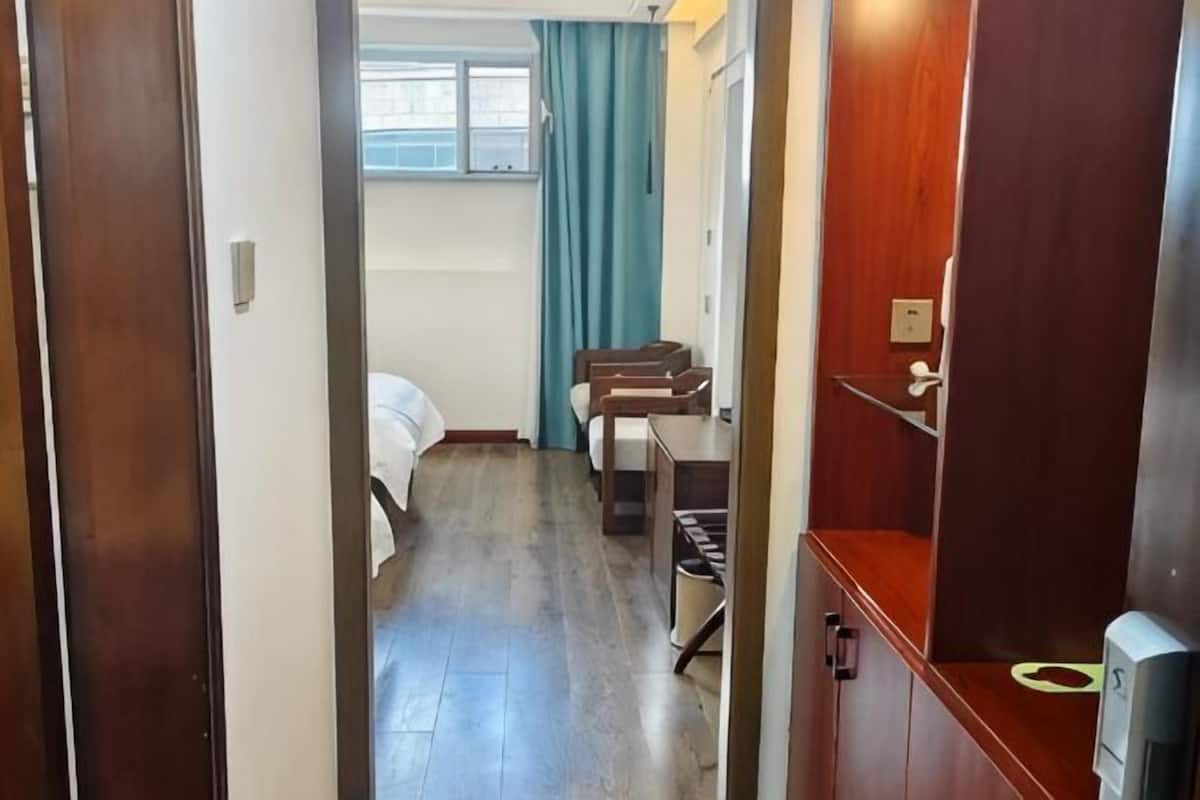 A narrow hallway leading to a bedroom with a bed, a desk, and a mirror.