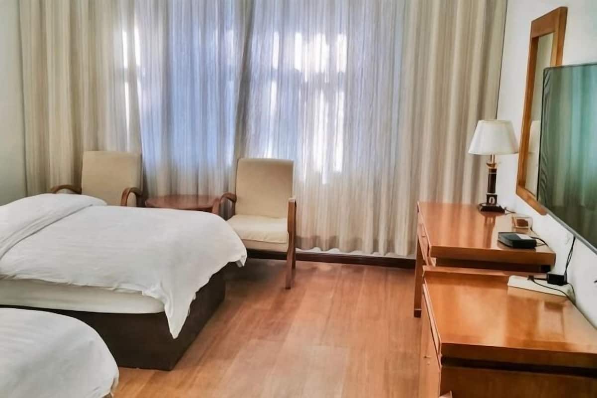Una habitación de hotel con dos camas, un escritorio con lámpara, una silla y un televisor.