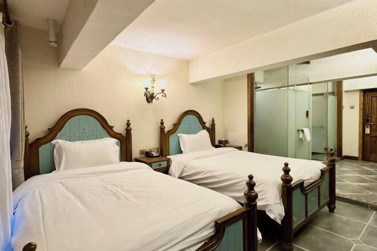 A hotel room with two beds, a mirror, a nightstand, and a wall-mounted light fixture.