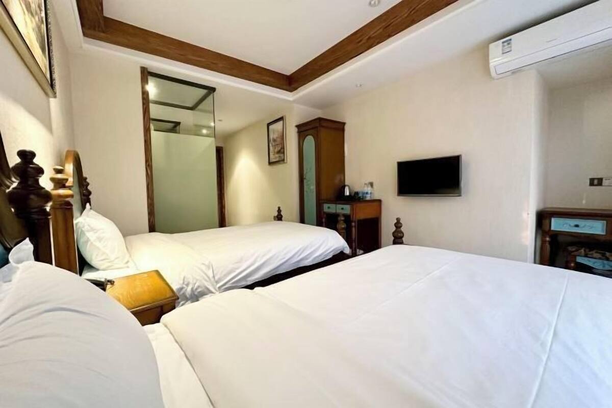 A hotel room with two beds, a television, a mirror, and a wooden ceiling.