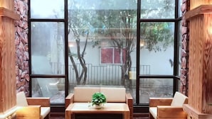 A room with large windows, a wooden bench, a table with a plant, and stone walls.