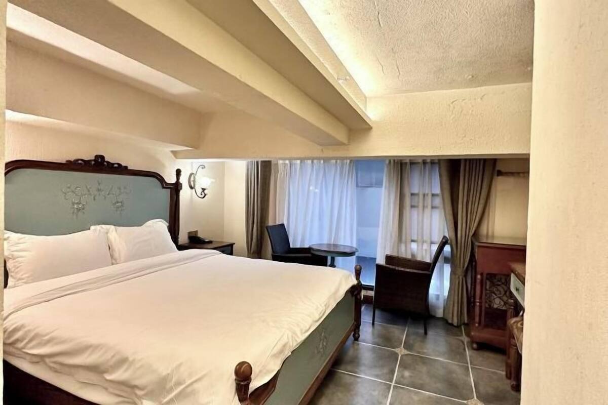 A hotel room with a large bed, a small table, and a chair.