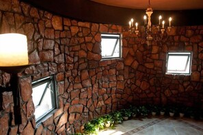 Une pièce avec un mur en pierre, un lustre et deux fenêtres.