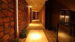 A hallway with stone walls and a tiled floor, leading to a room with a large window.