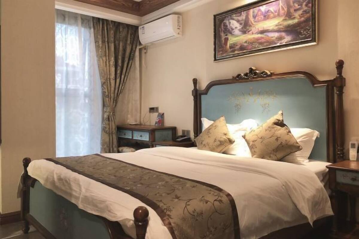 A bedroom with a bed, a nightstand, a dresser, a painting on the wall, and an air conditioning unit.