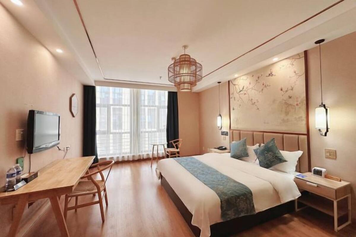 A hotel room with a bed, a desk, a chair, a TV, and a window.