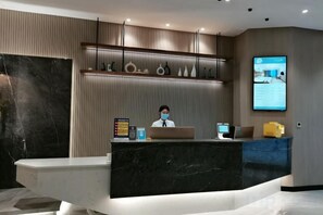 A reception desk with a receptionist, a computer, and a digital screen displaying information. - Jingan Hotel (Shaoxing Keqiao Yintai Lantian Shixin Plaza) (Shaoxing)