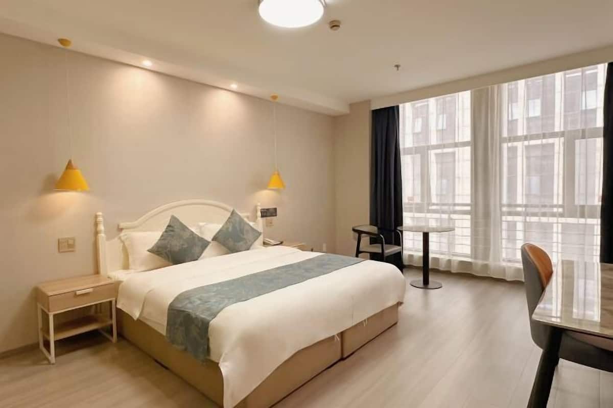 A hotel room with a bed, bedside tables, a small table, and a chair.