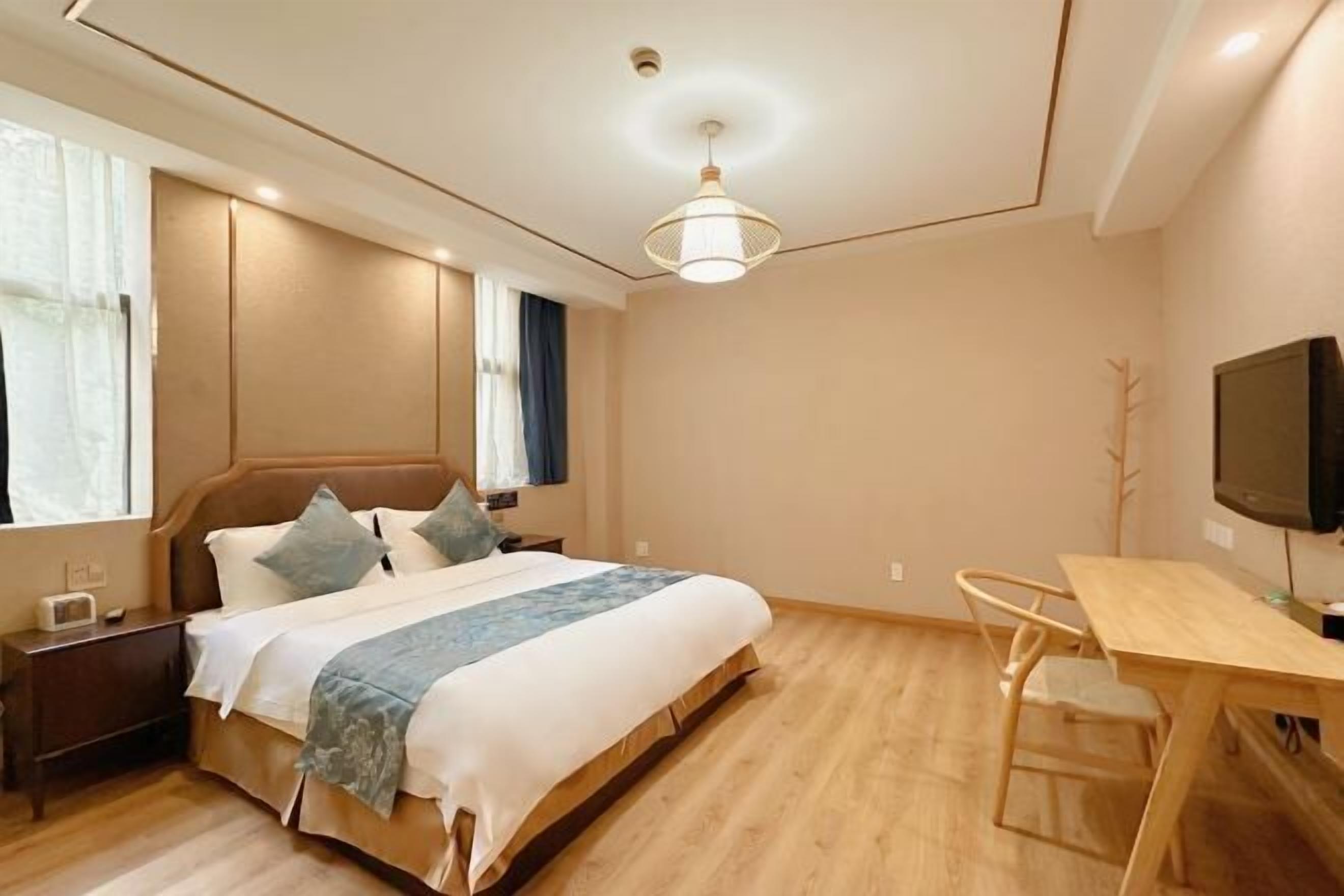 A bedroom with a bed, bedside table, TV, and a desk with a chair.