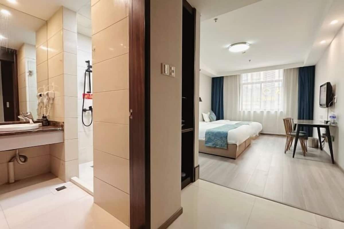 A hotel room with a bathroom, a bed, a desk, and a window.