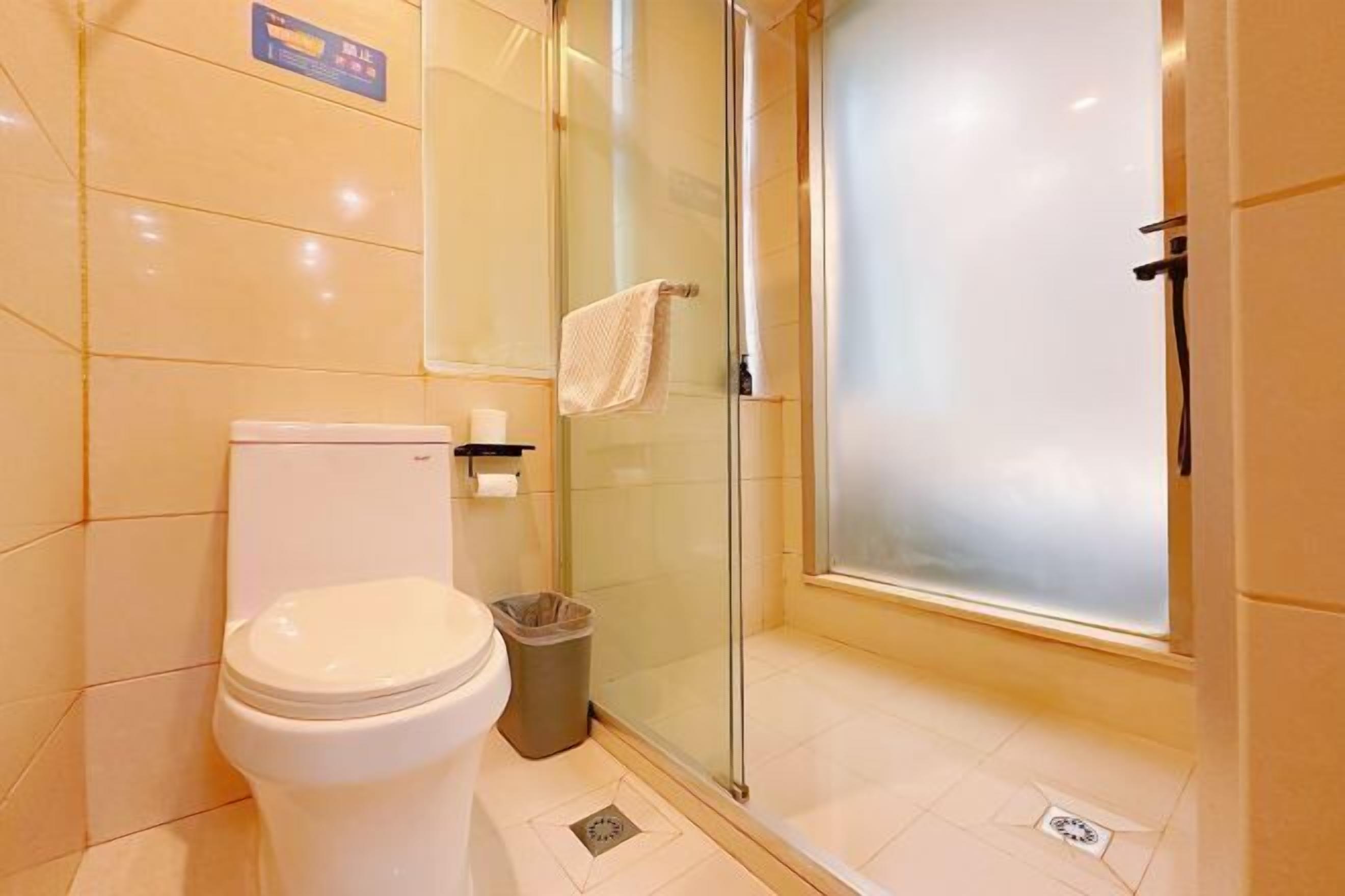 A bathroom with a toilet, a glass shower enclosure, a towel hanging on the wall, and a trash bin.