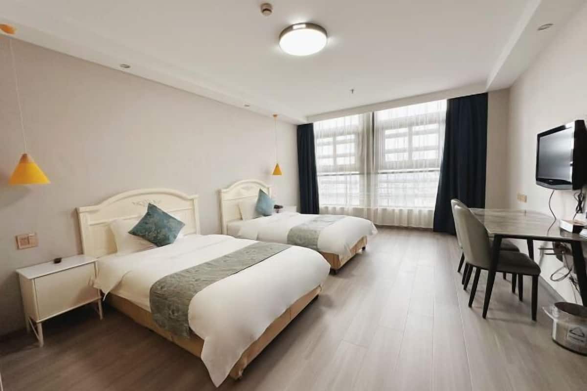 A hotel room with two beds, a desk, a TV, and a window with curtains.