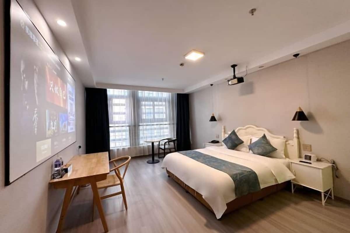 A hotel room with a bed, bedside table, lamp, and a desk with a chair.